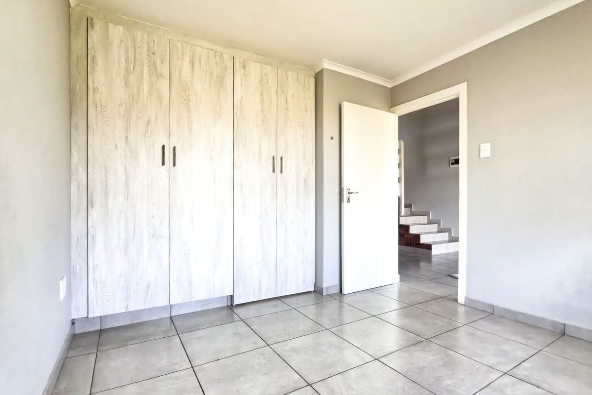 A clean, empty bedroom featuring light-toned built-in cupboards and neutral tiled flooring, offering a versatile space ready for personalization.