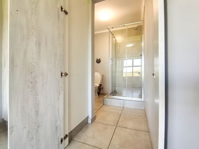A clean and functional bathroom featuring a glass-enclosed shower, tiled flooring, and a standard toilet, presented in a neutral, well-maintained condition.