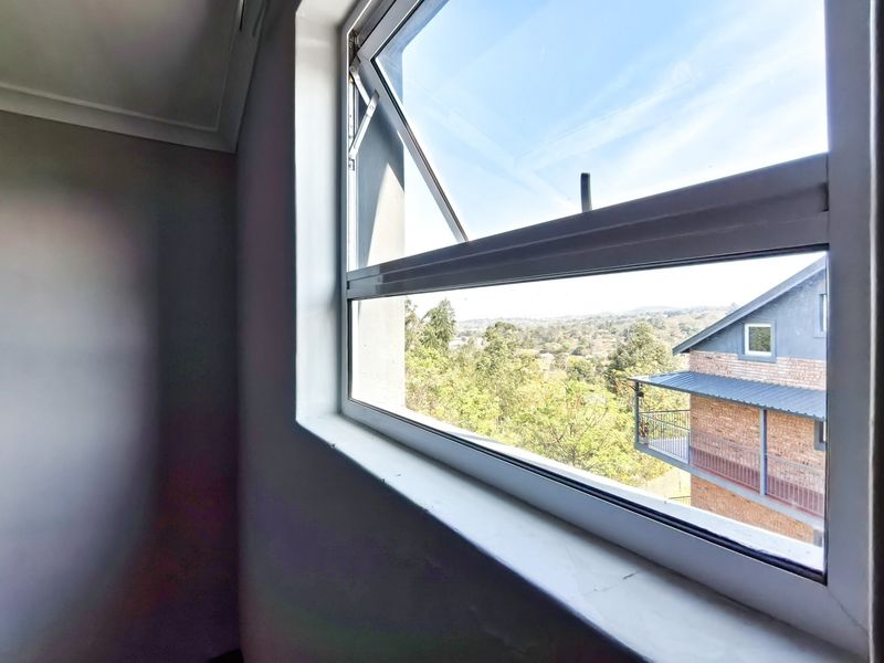 A bright, empty bedroom featuring a top-hung aluminium window with scenic neighbourhood views and clean, neutral wall finishes.