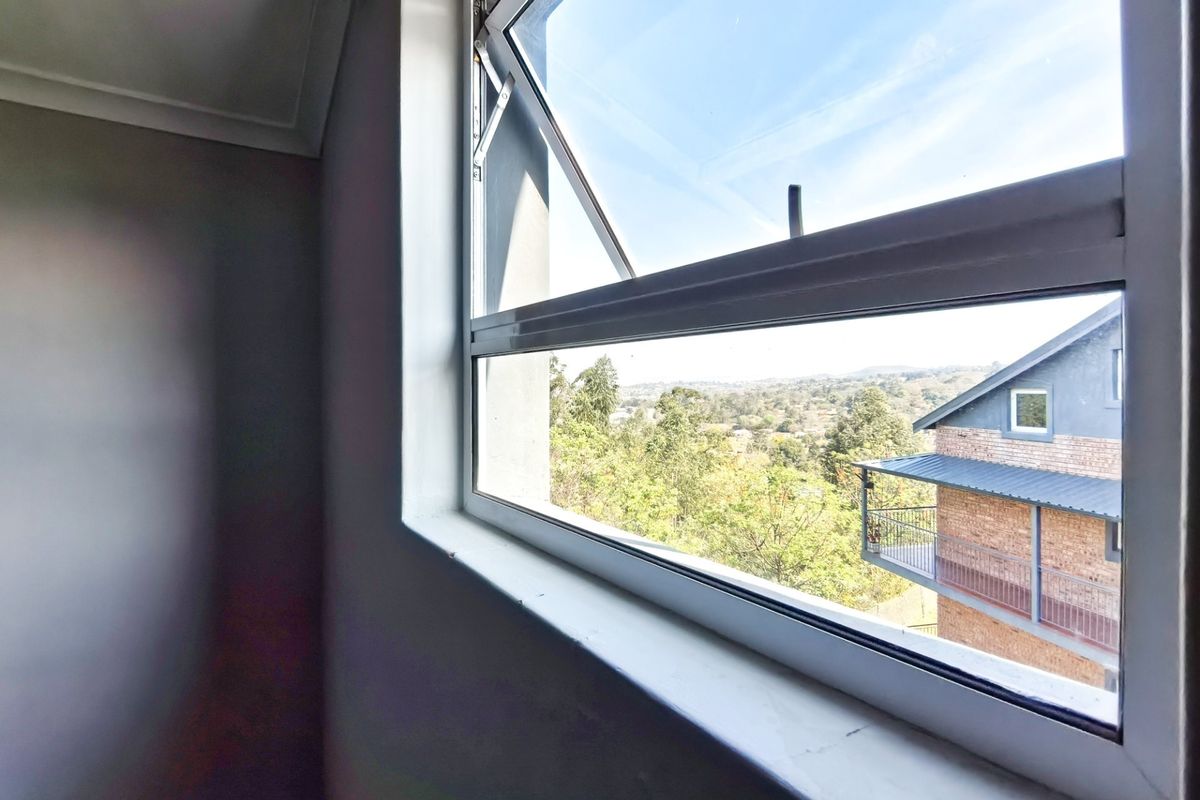 A bright, empty bedroom featuring a top-hung aluminium window with scenic neighbourhood views and clean, neutral wall finishes.