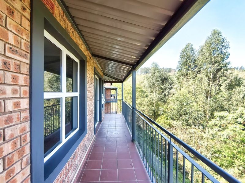 A spacious covered balcony featuring tiled flooring, a secure metal balustrade, and views of the surrounding trees.