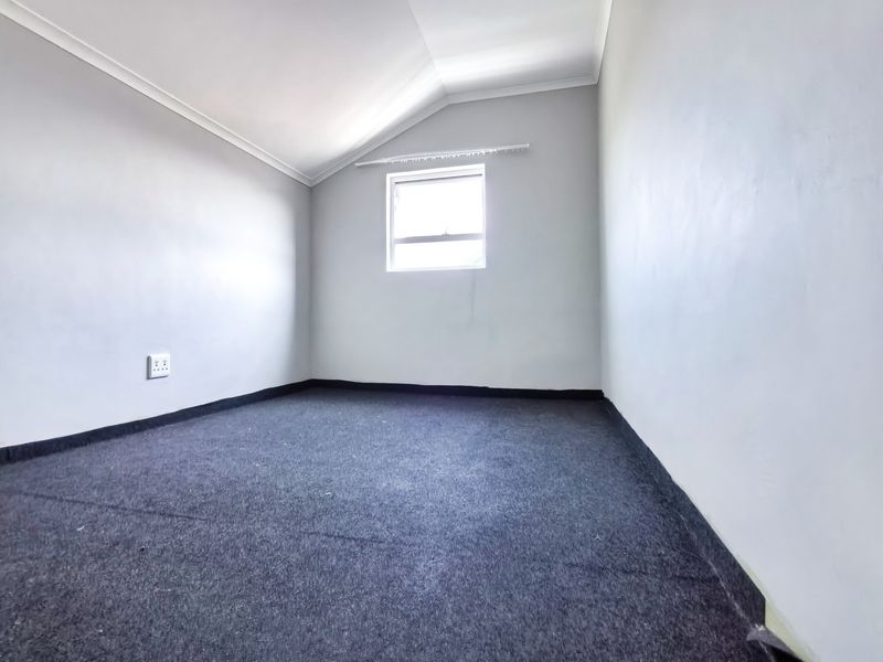 An empty bedroom featuring a sloped ceiling, grey carpeting, and a single window with a curtain rail.
