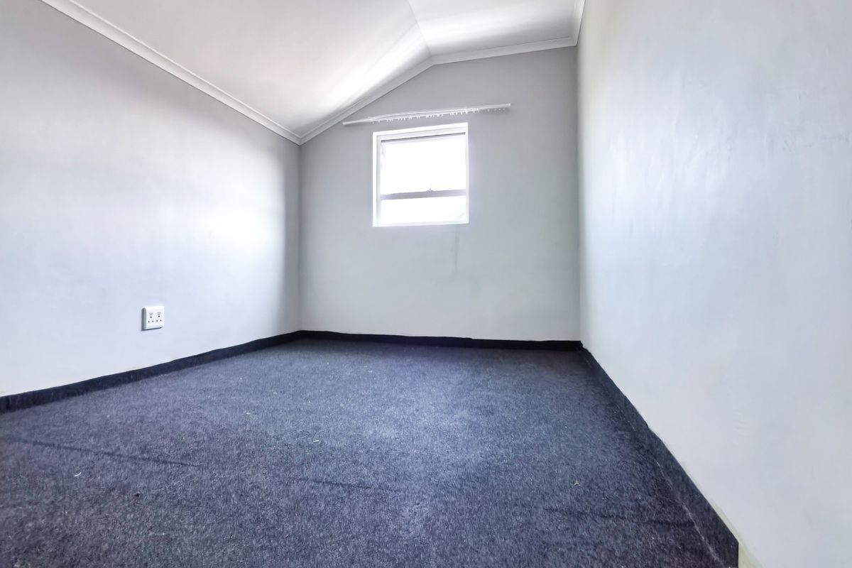 An empty bedroom featuring a sloped ceiling, grey carpeting, and a single window with a curtain rail.