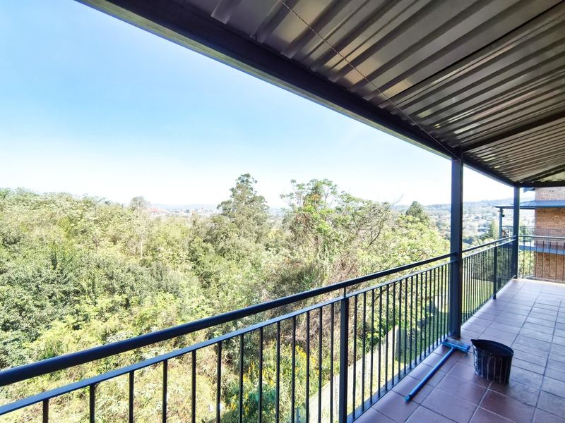 A spacious covered balcony featuring tiled flooring and metal railings, offering expansive views of the surrounding greenery.