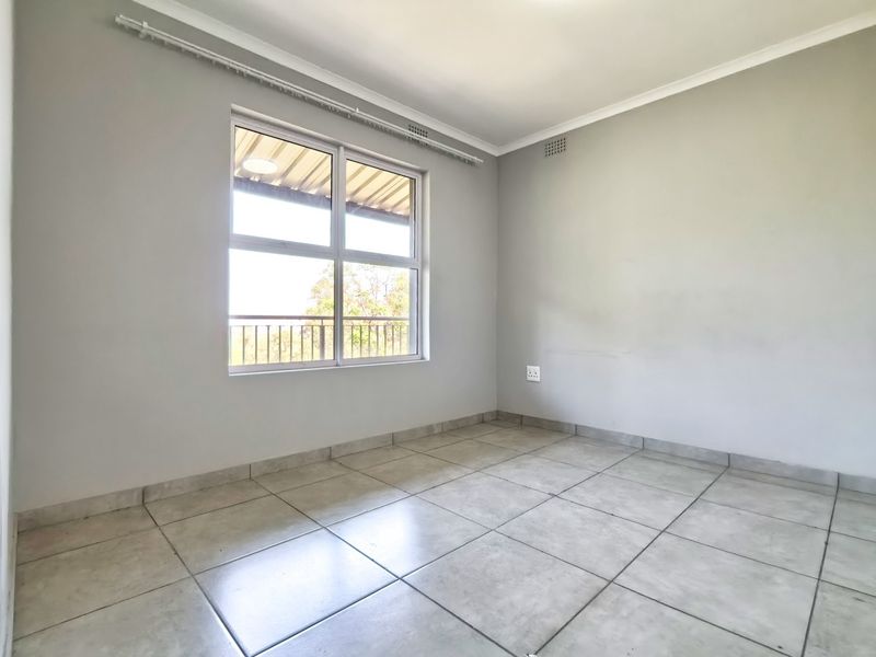 A bright, empty bedroom featuring neutral tiled flooring, clean walls, and a large window providing natural light.