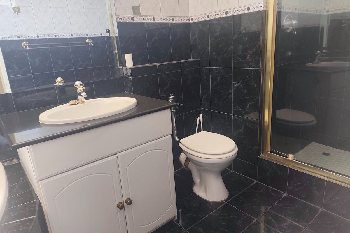 A functional bathroom featuring a vanity cabinet with integrated sink, toilet, and a shower enclosure with dark tiled finishes.