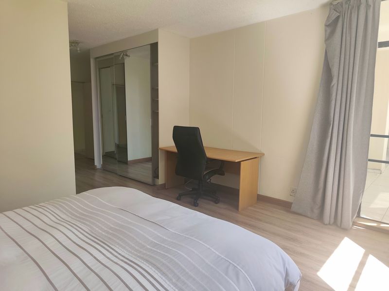A bedroom featuring laminate flooring, a built-in mirrored wardrobe, and direct access to a balcony through a sliding glass door.