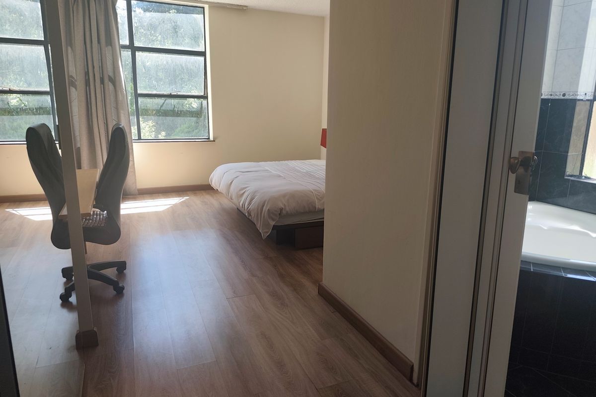 Spacious bedroom featuring laminate flooring, large windows for natural light, and direct access to an en-suite bathroom with a built-in bathtub.