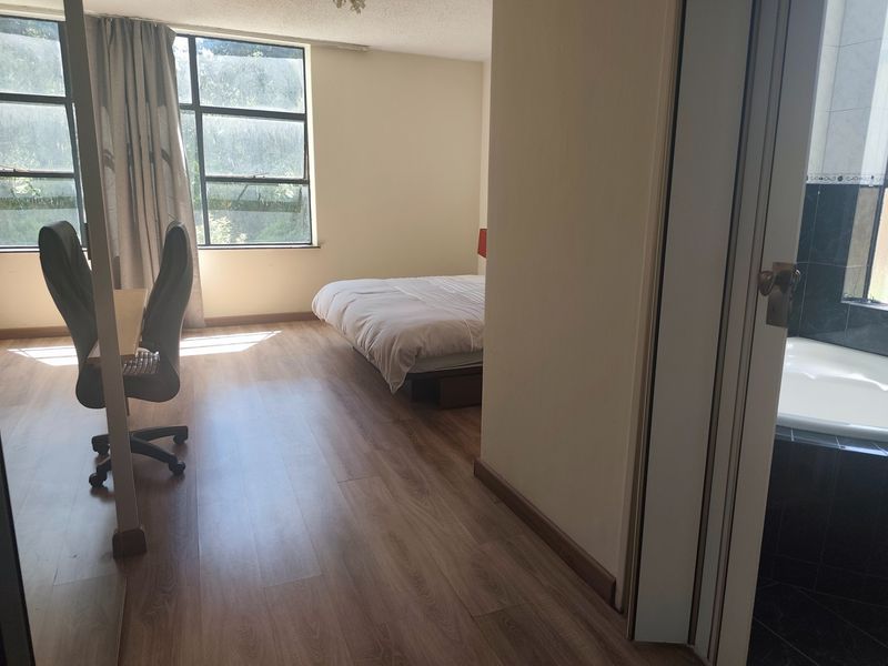 Spacious bedroom featuring laminate flooring, large windows for natural light, and direct access to an en-suite bathroom with a built-in bathtub.