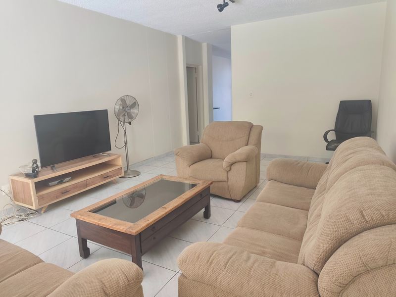 A living room featuring tiled flooring, popcorn ceiling, and track lighting, providing a functional space for relaxation.
