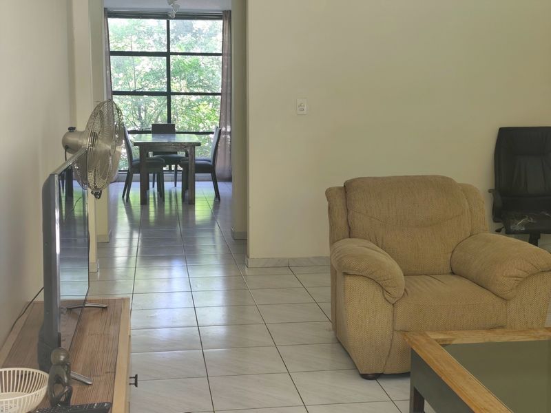 Open plan living and dining area featuring tiled flooring and a large window providing natural light and garden views.
