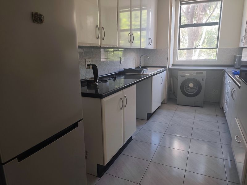 A functional kitchen featuring white cabinetry, dark granite countertops, tiled flooring, and a dedicated space for a washing machine under the counter.