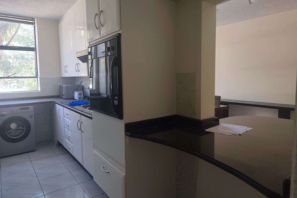 A functional kitchen featuring white cabinetry, dark granite countertops, a built-in oven, and a breakfast bar, with tiled flooring and natural light.