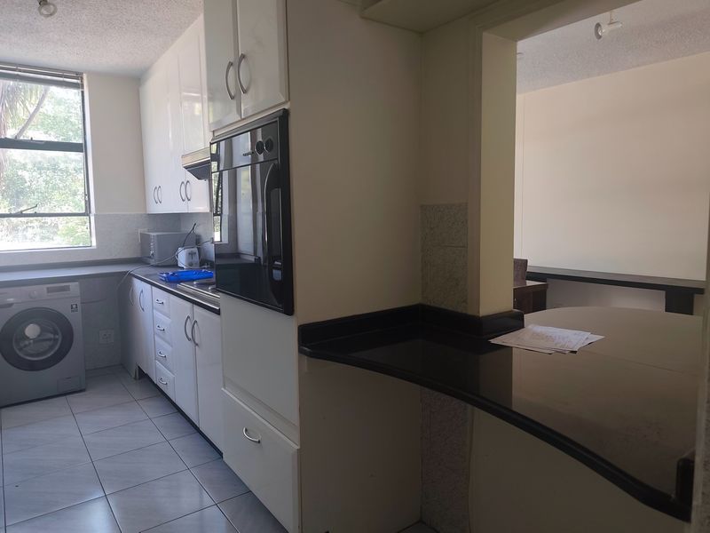 A functional kitchen featuring white cabinetry, dark granite countertops, a built-in oven, and a breakfast bar, with tiled flooring and natural light.