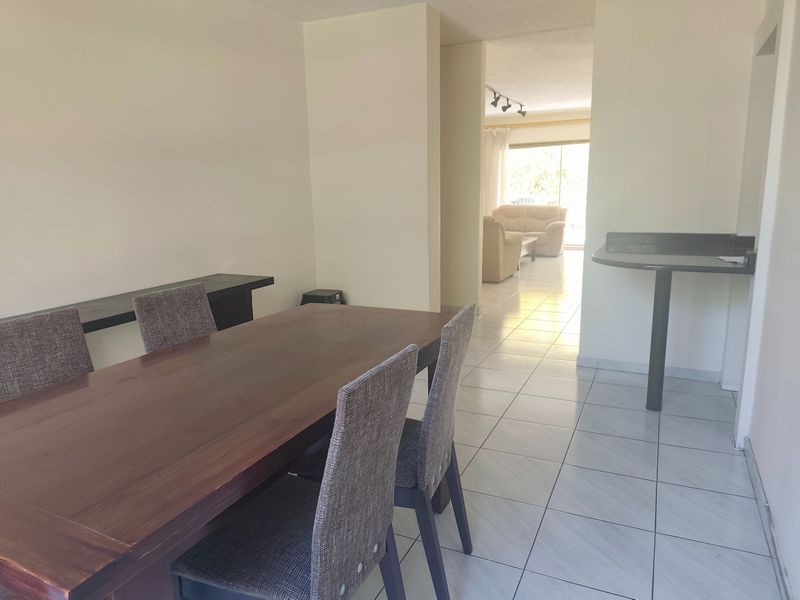 Open plan dining and living area featuring tiled flooring, a breakfast bar, and natural light flowing through to the rear patio.