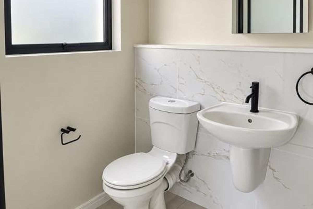 A modern, clean bathroom featuring a wall-mounted basin, toilet, marble-look wall tiling, and contemporary black fixtures.