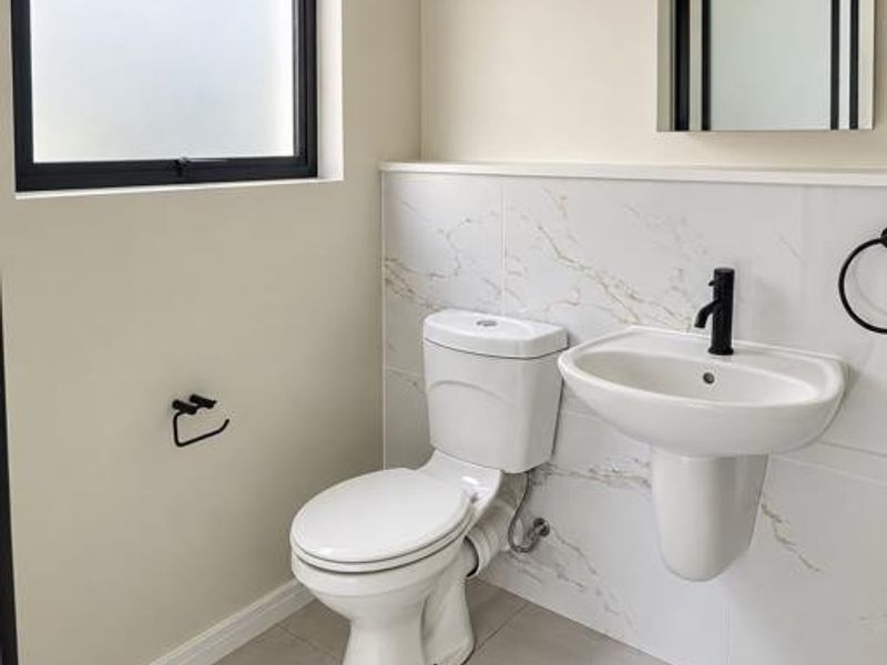 A modern, clean bathroom featuring a wall-mounted basin, toilet, marble-look wall tiling, and contemporary black fixtures.