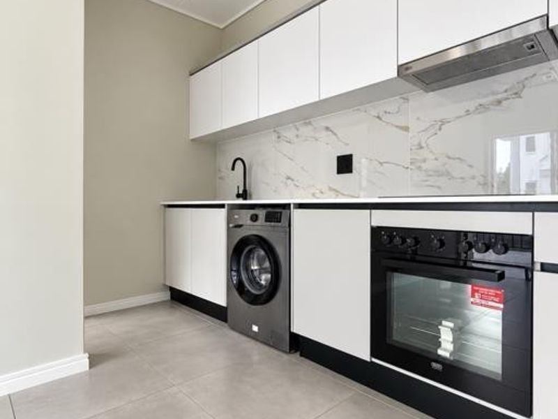 A modern, minimalist kitchen featuring sleek white cabinetry, a marble-look splashback, integrated appliances, and neutral tiled flooring.