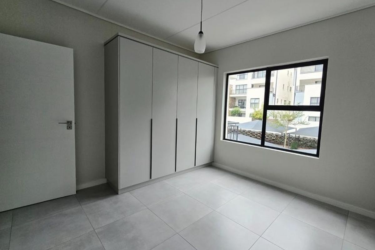 A bright, modern bedroom featuring neutral tiled flooring, a large built-in wardrobe, and a contemporary pendant light fixture.