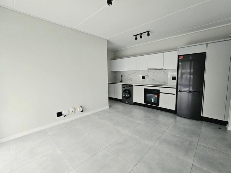 Modern open-plan kitchen featuring sleek white cabinetry, marble-look splashback, integrated appliances, and contemporary tiled flooring in a bright, minimalist space.