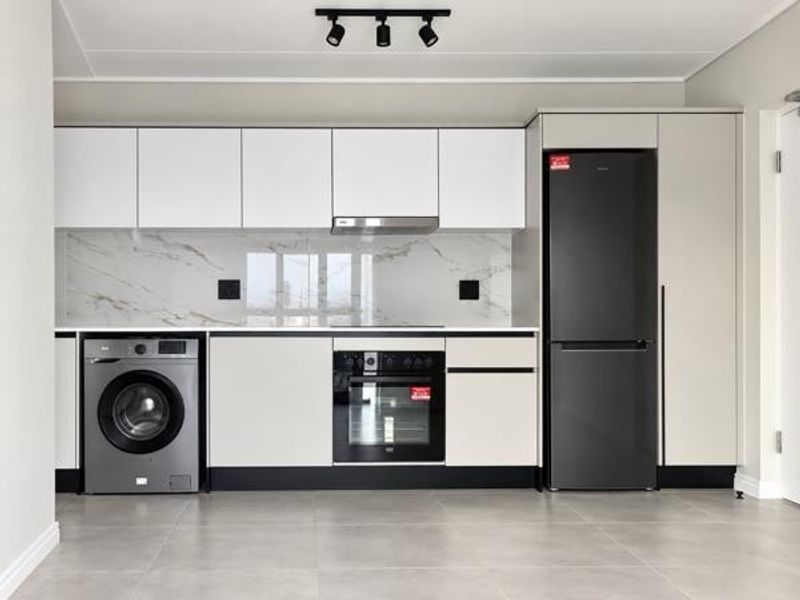 Modern kitchen featuring sleek white cabinetry, marble-look splashback, integrated oven, extractor fan, and contemporary track lighting in a clean, minimalist space.
