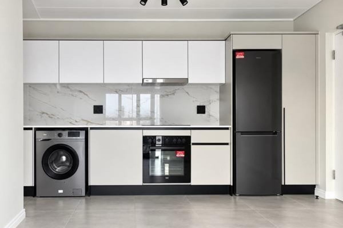 Modern kitchen featuring sleek white cabinetry, marble-look splashback, integrated oven, extractor fan, and contemporary track lighting in a clean, minimalist space.