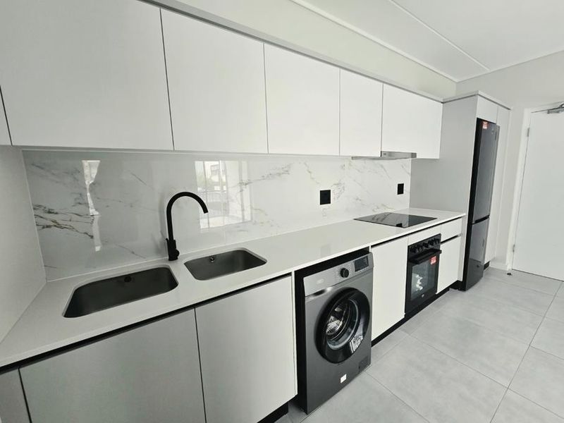 Modern, minimalist kitchen featuring sleek white cabinetry, marble-look splashback, quartz countertops, and integrated appliances including an oven, hob, and washing machine.