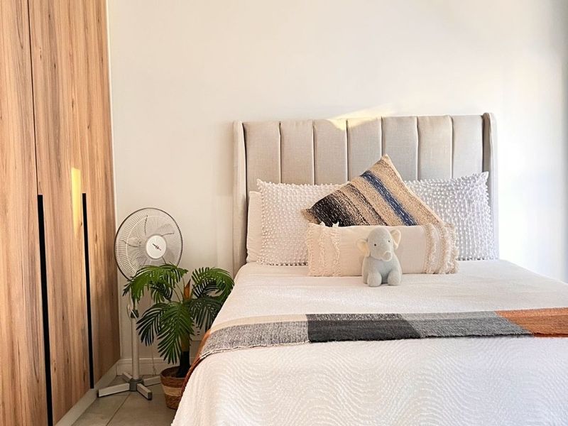 A well-maintained bedroom featuring modern wood-finish built-in wardrobes, neutral tiled flooring, and a contemporary pendant light fixture.