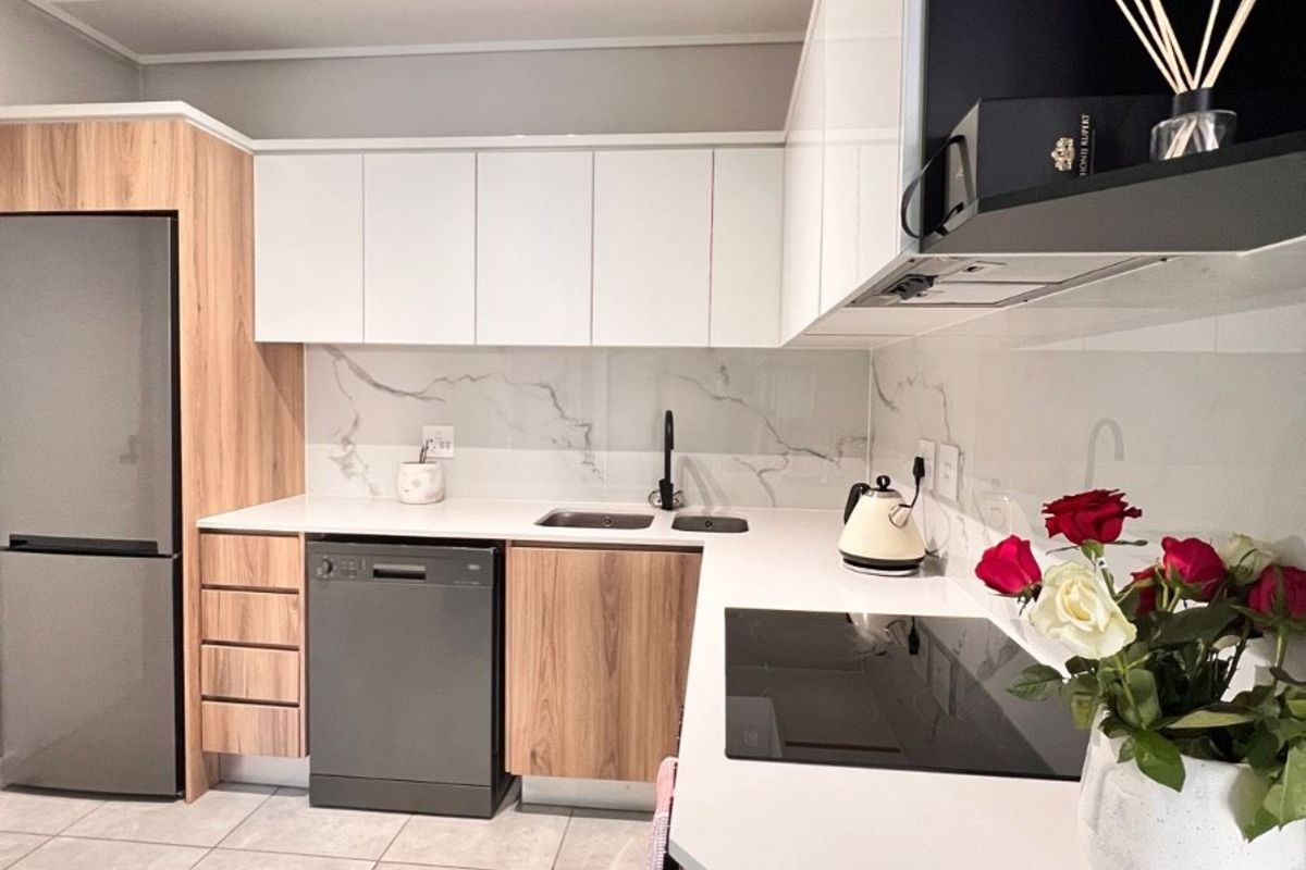 Modern kitchen featuring sleek two-tone cabinetry, stone countertops, marble-look splashback, integrated hob, and high-quality finishes throughout.