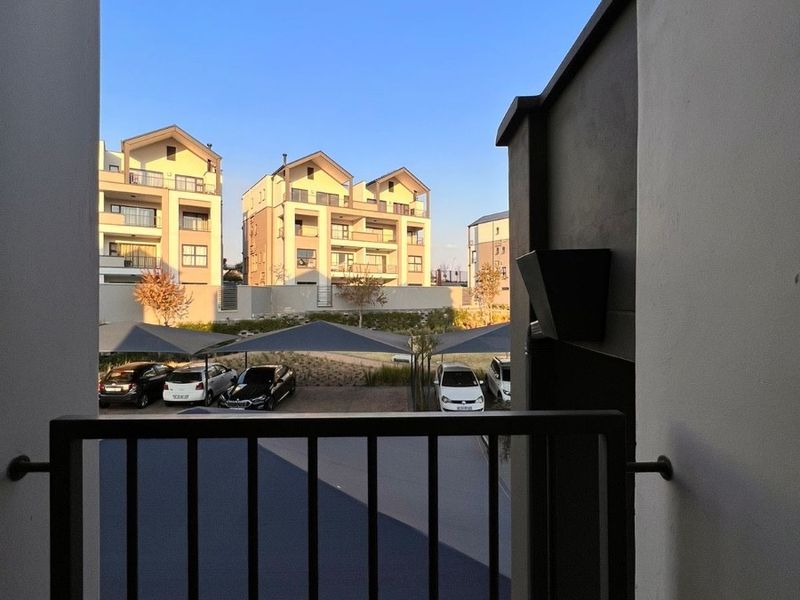 A view from a balcony overlooking a parking area with shade sails and surrounding apartment buildings.