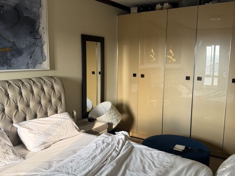 A well-maintained bedroom featuring modern high-gloss built-in cupboards and decorative crown molding, providing ample storage and a clean aesthetic.