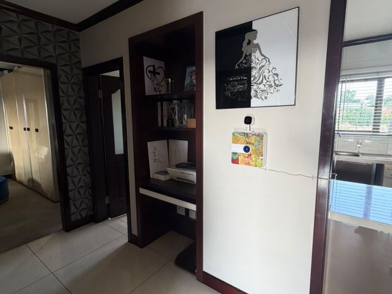A well-maintained hallway featuring tiled flooring, dark wood trim, and a built-in recessed desk or shelving unit with a textured feature wall.