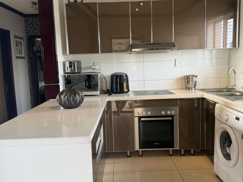 Modern kitchen featuring glossy brown cabinetry, white stone countertops, integrated oven, electric hob, and tiled flooring with a functional layout.