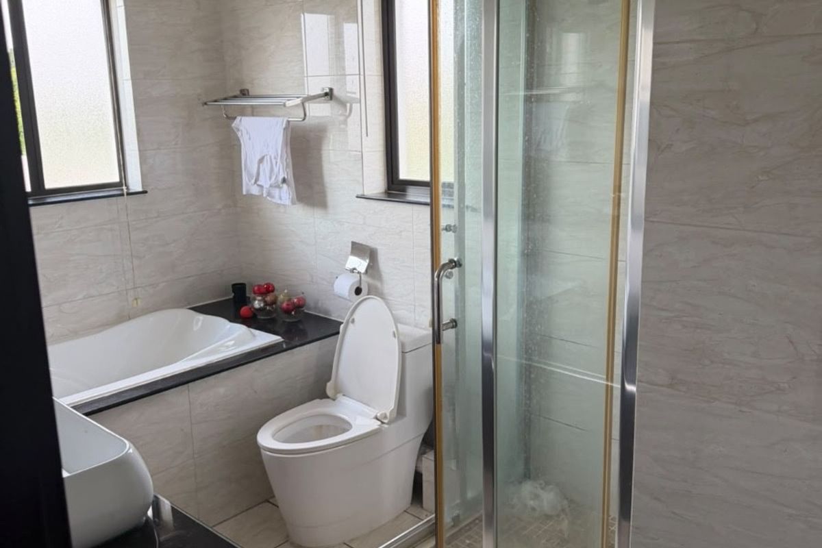 A functional bathroom featuring a built-in bathtub, separate shower enclosure, toilet, and vanity basin with tiled finishes throughout.