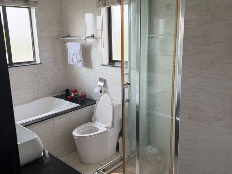 A functional bathroom featuring a built-in bathtub, separate shower enclosure, toilet, and vanity basin with tiled finishes throughout.