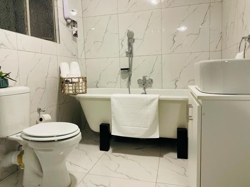 A compact bathroom featuring marble-look wall and floor tiles, a freestanding bathtub with shower mixer, and a modern vessel sink vanity.