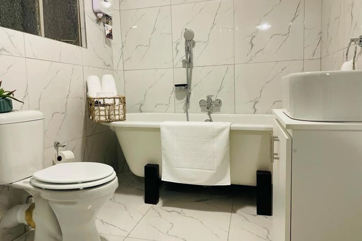 A compact bathroom featuring marble-look wall and floor tiles, a freestanding bathtub with shower mixer, and a modern vessel sink vanity.