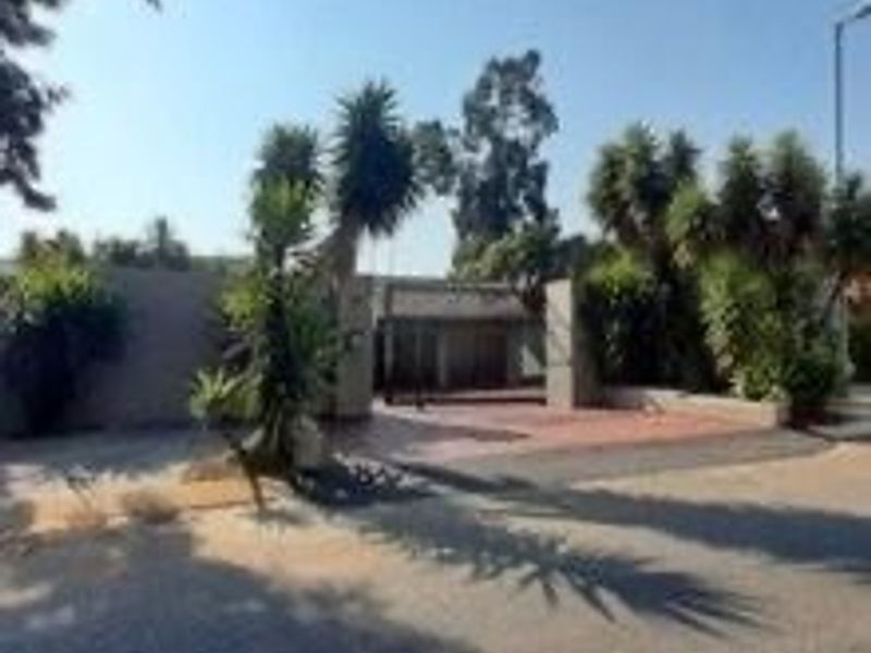 Front exterior view of the apartment complex featuring a paved driveway, boundary wall, and entrance area with established landscaping.