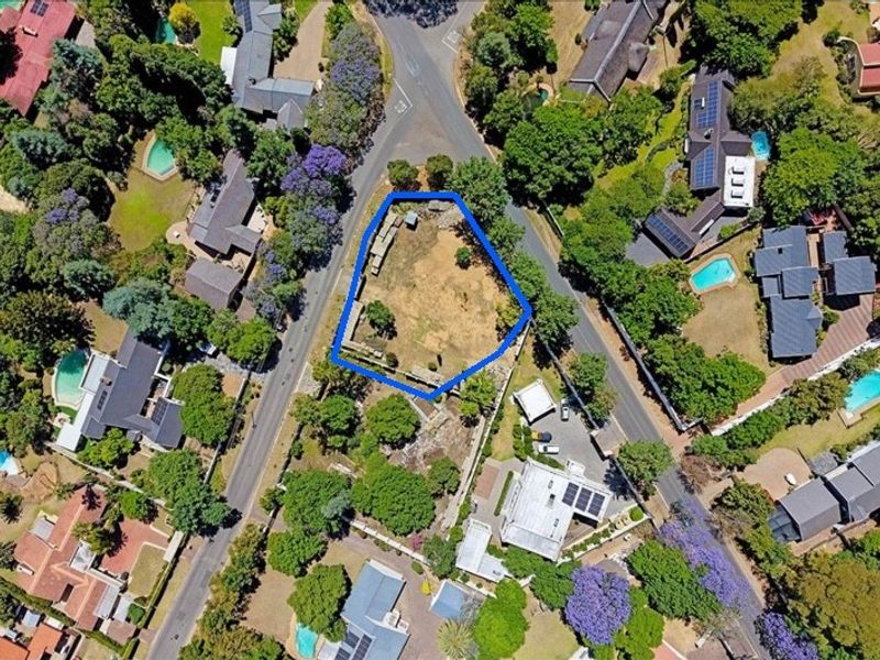 Aerial view of a vacant residential plot highlighted in blue, situated within an established suburban neighborhood with mature trees and surrounding properties.