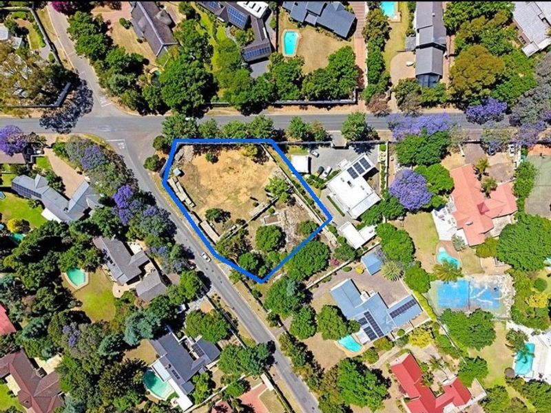 An aerial view of a vacant residential plot featuring established trees and boundary fencing, situated in a well-developed suburban neighborhood.