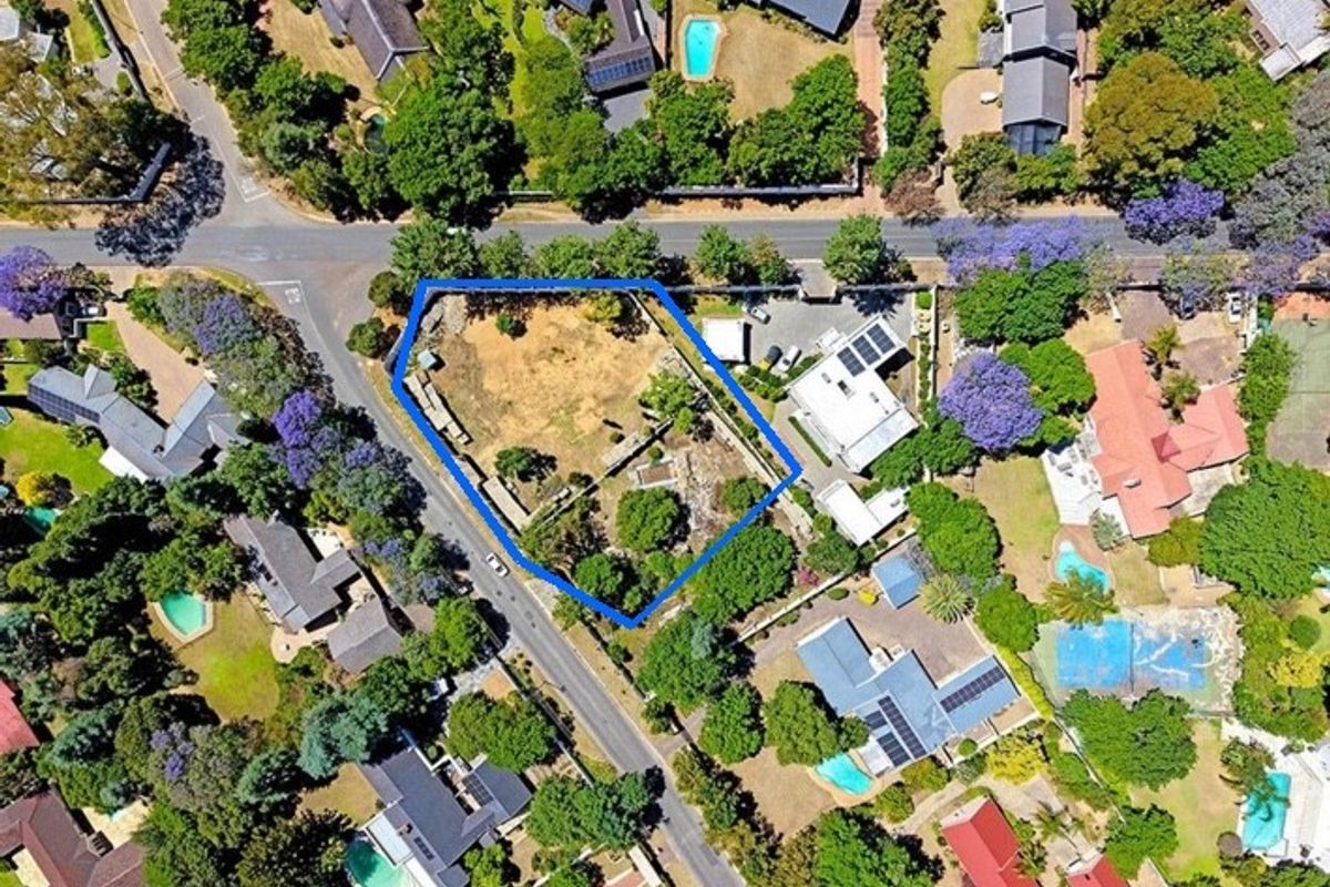 An aerial view of a vacant residential plot featuring established trees and boundary fencing, situated in a well-developed suburban neighborhood.