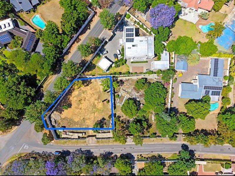 Aerial view of a vacant residential plot featuring perimeter fencing and established trees, situated in a developed suburban neighborhood.