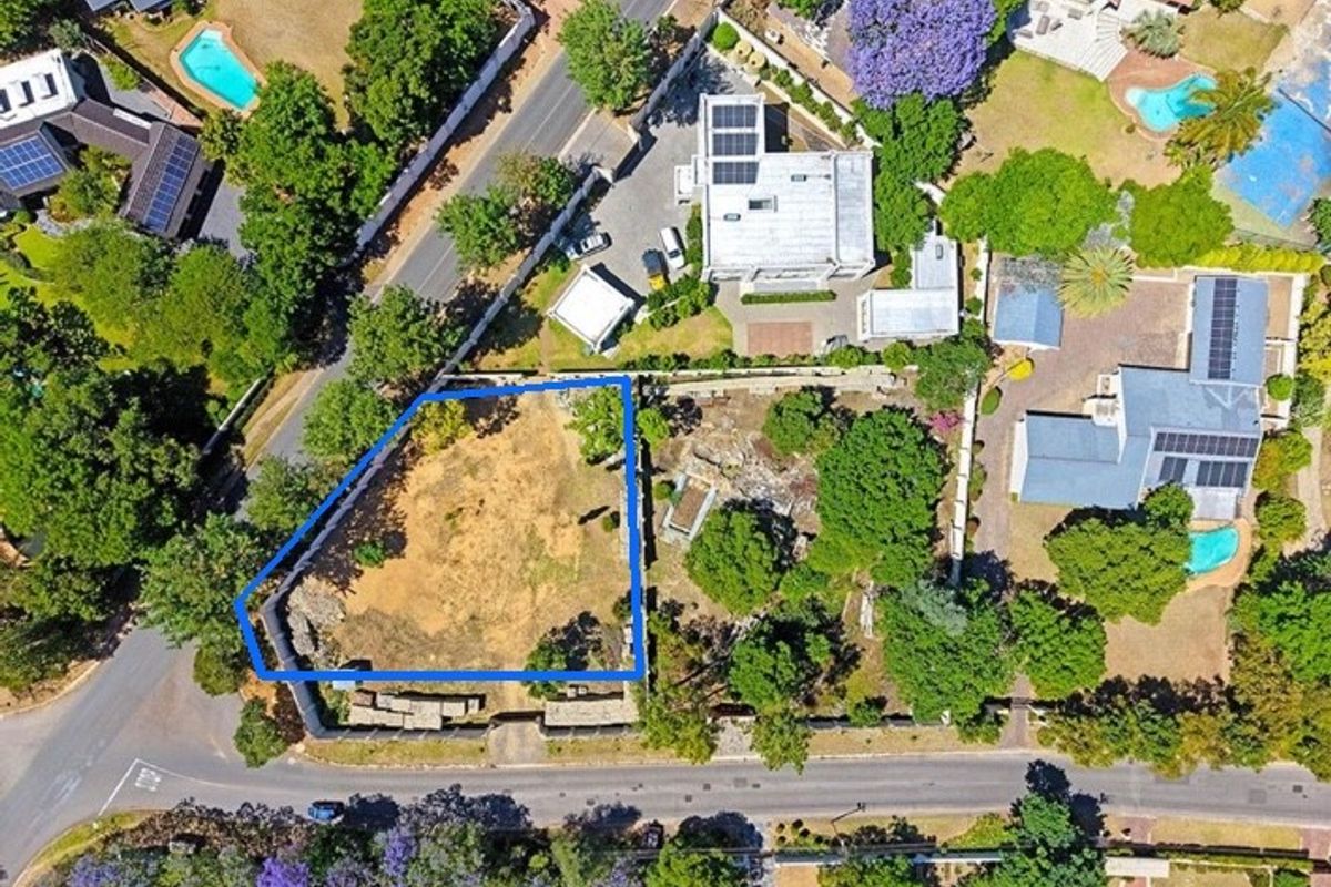 Aerial view of a vacant residential plot featuring perimeter fencing and established trees, situated in a developed suburban neighborhood.