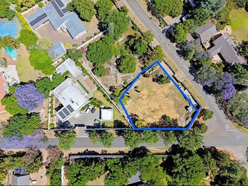 Aerial view of a vacant residential plot highlighted in blue, situated in a well-established neighborhood with mature trees and street access.