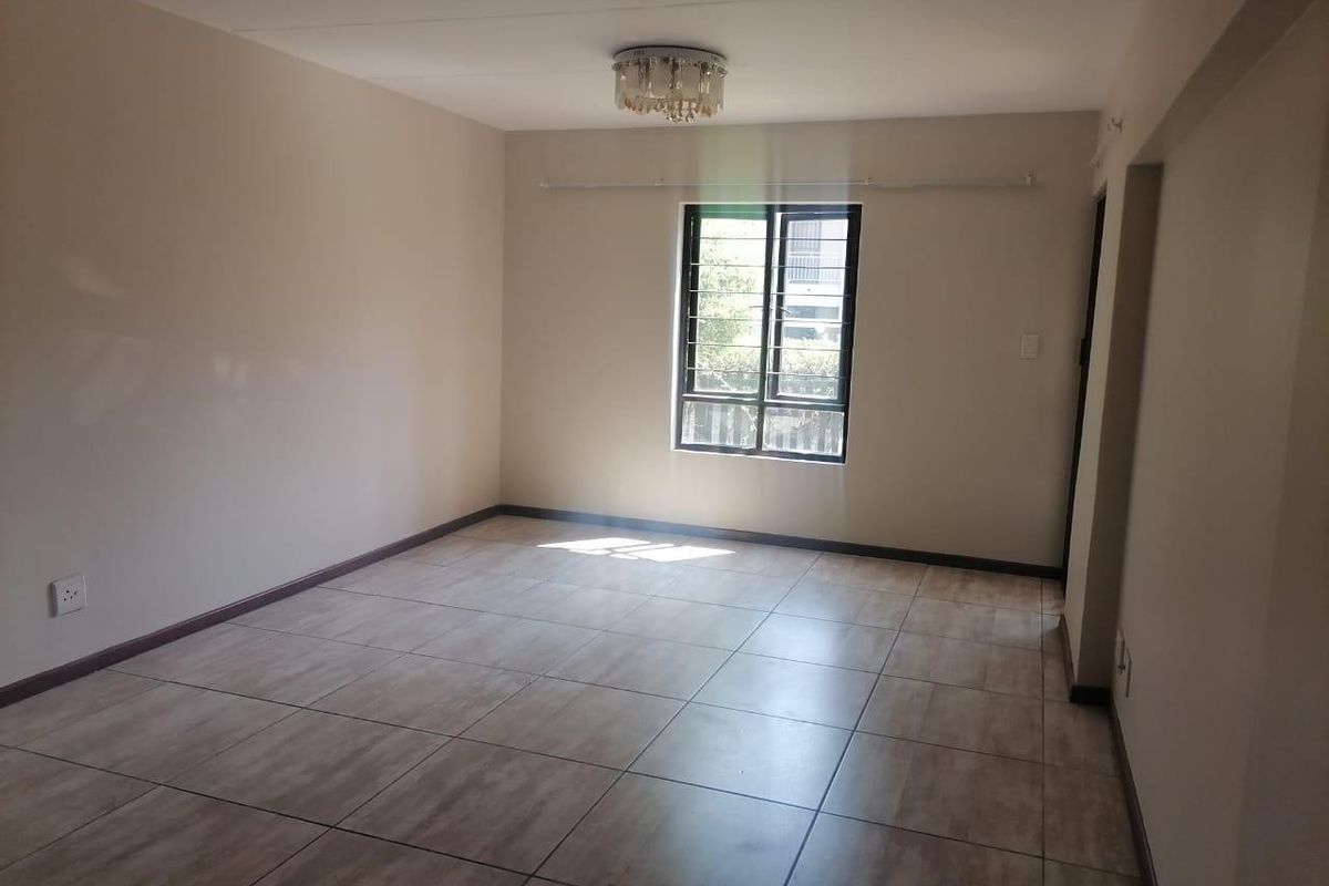 A bright, empty living room featuring neutral walls, tiled flooring, and a window with security bars, offering a clean canvas for personalization.