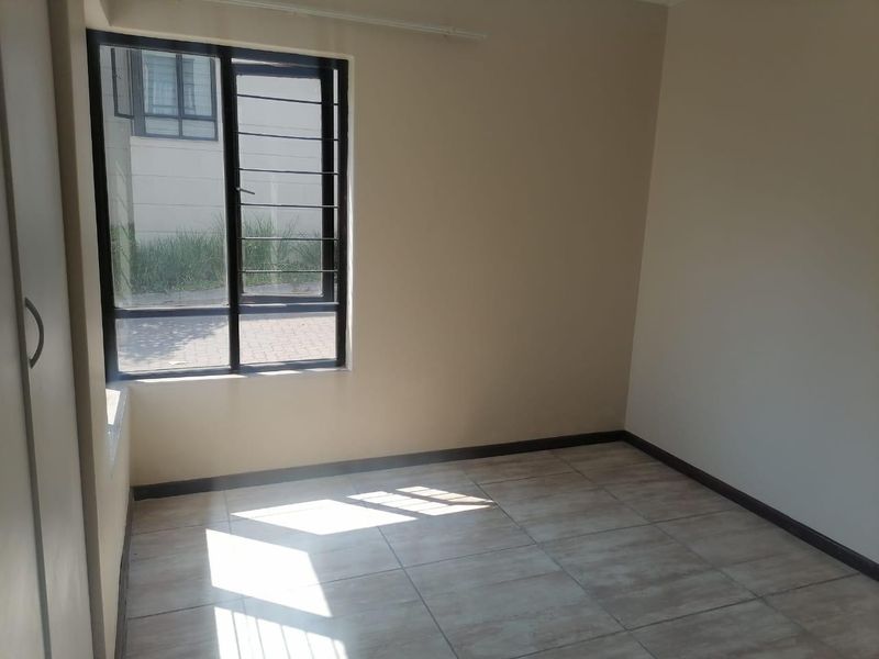 A bright, empty bedroom featuring neutral walls, tiled flooring, and a built-in cupboard with security bars on the window.