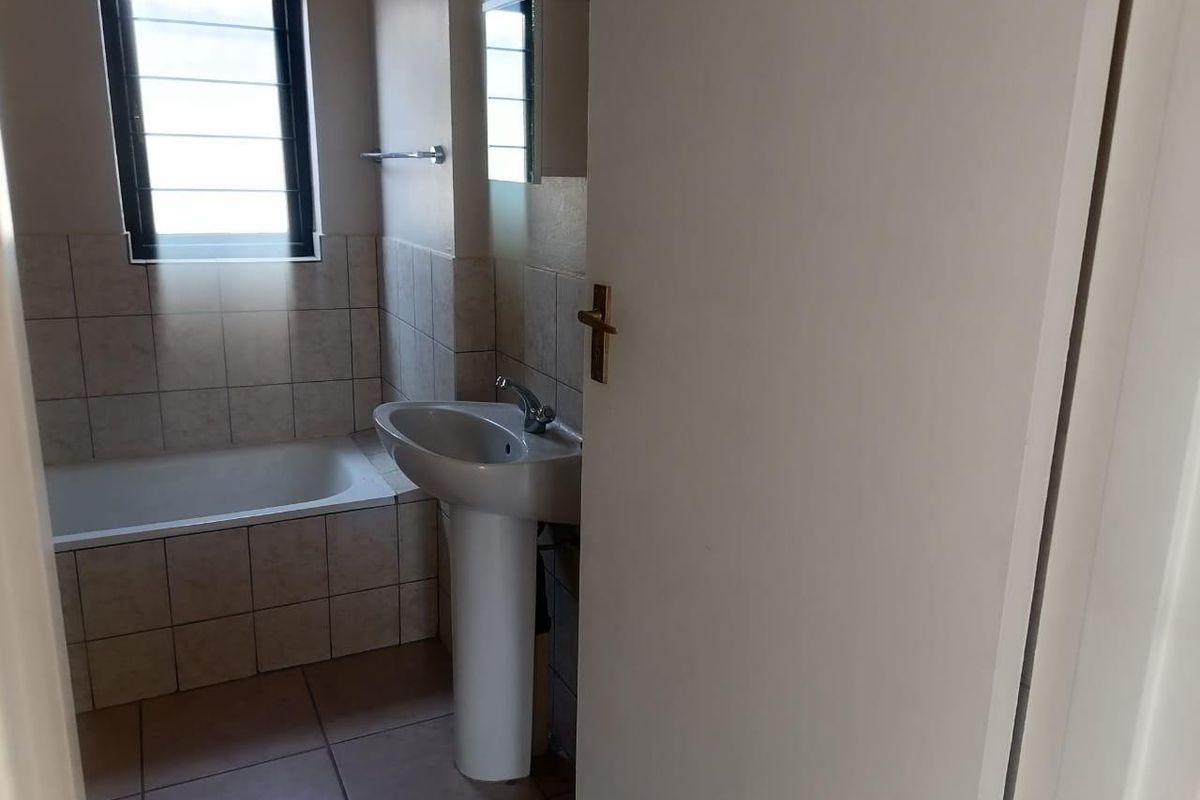 A functional bathroom featuring a pedestal basin, a built-in bathtub, and neutral wall and floor tiling.