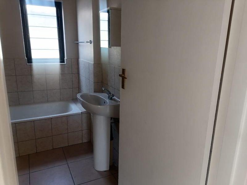 A functional bathroom featuring a pedestal basin, a built-in bathtub, and neutral wall and floor tiling.