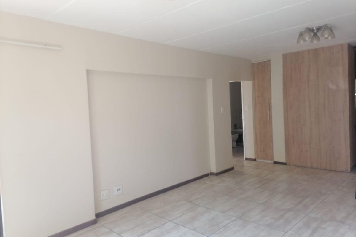 A spacious, empty bedroom featuring neutral wall tones, tiled flooring, and built-in wooden cupboards, offering a clean and versatile living space.