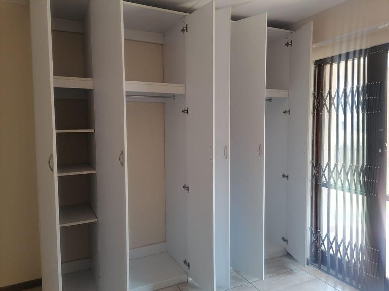 A bedroom featuring white built-in wardrobes with shelving and hanging space, tiled flooring, and a security gate leading to an outdoor area.